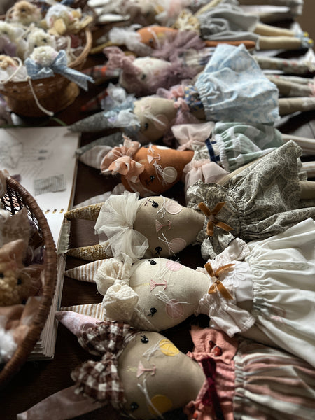 Collection of handmade dolls with various outfits and accessories on a table.