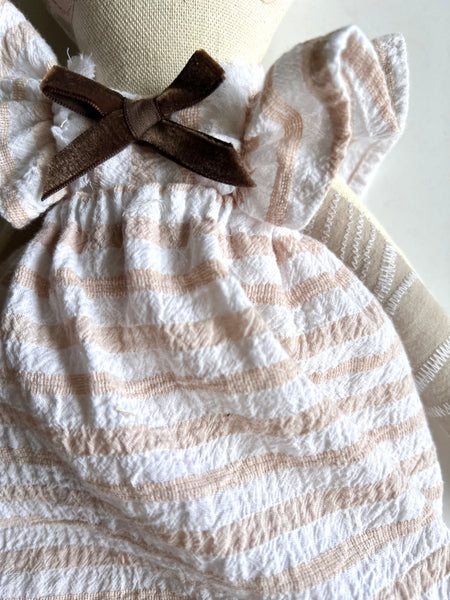 White dress with brown stripes and a bow on a cat doll against a neutral background