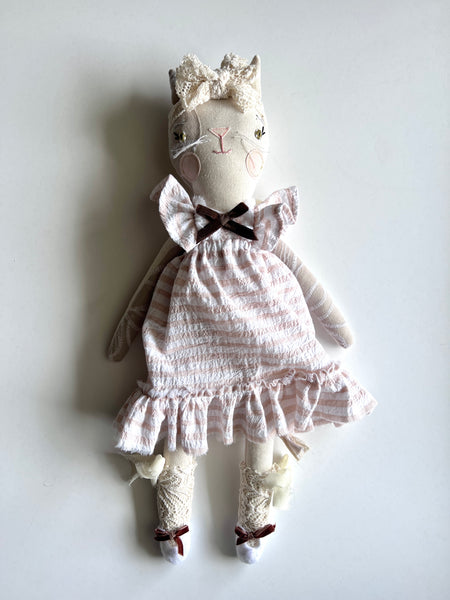 Textile cat doll with a white dress and bow on a light gray background