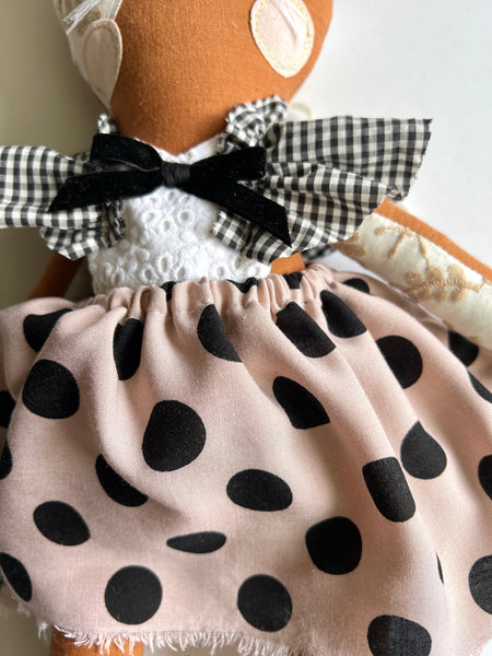 Doll wearing a polka dot dress with a checkered bow