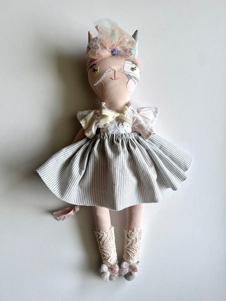 Cat doll dressed in a handmade dress with ruffles on a plain background