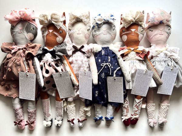 Row of handcrafted dolls with various outfits on a white background