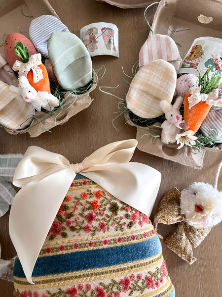 Decorative Easter egg with floral pattern and bow, surrounded by small Easter decorations on a wooden surface.