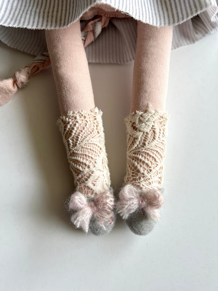 Close-up of feet wearing beige knitted socks with pom-poms on a light background