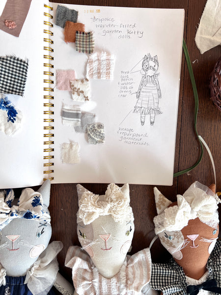 Notebook with cat sketches and fabric samples on a wooden surface.