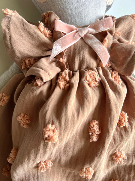 Beige dress with floral details on doll against a neutral background.