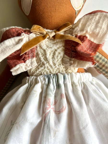 Close-up of a doll with a white dress and red accents, sitting on a surface.