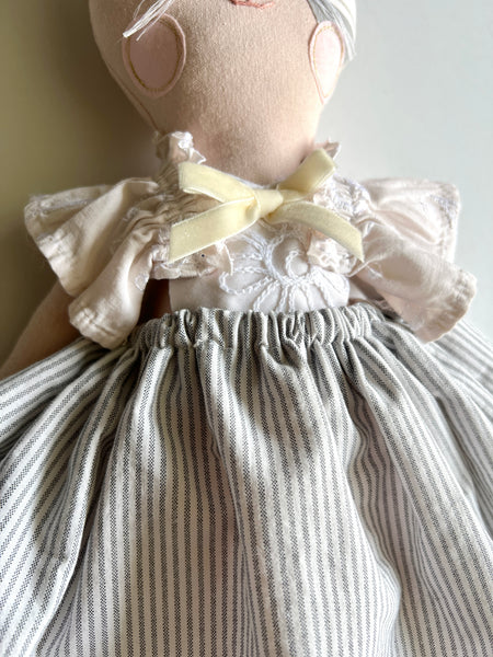 Textile doll with a white blouse and striped skirt on a plain background